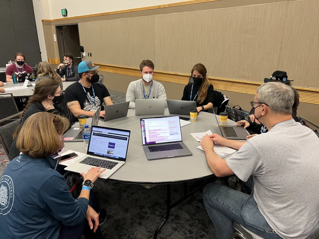 Folks sitting around a table with computers writing code.