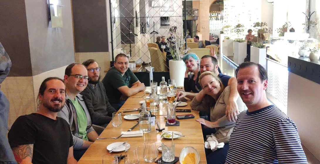 Group of 8ish people sitting a table smiling and looking at the camera