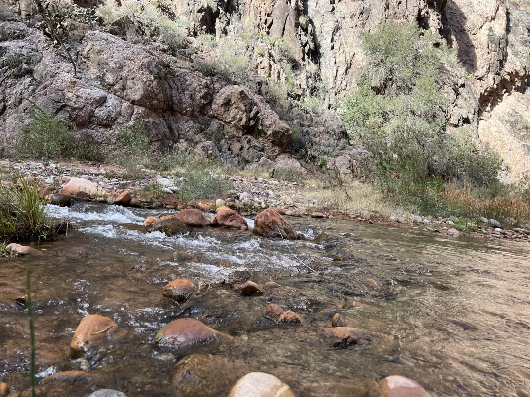 Narrow rocky and shallow stream with canyon wall on the other side