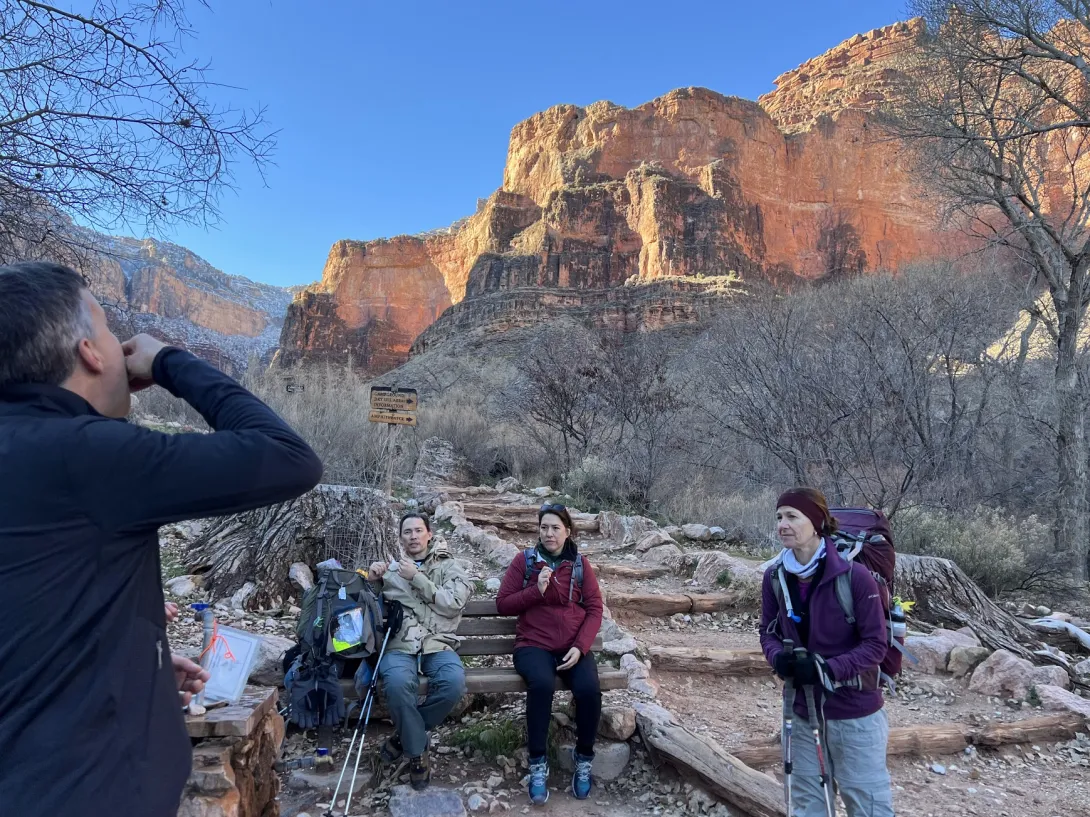 Group of people sitting down and resting on the trail with the canyon wall in the background.