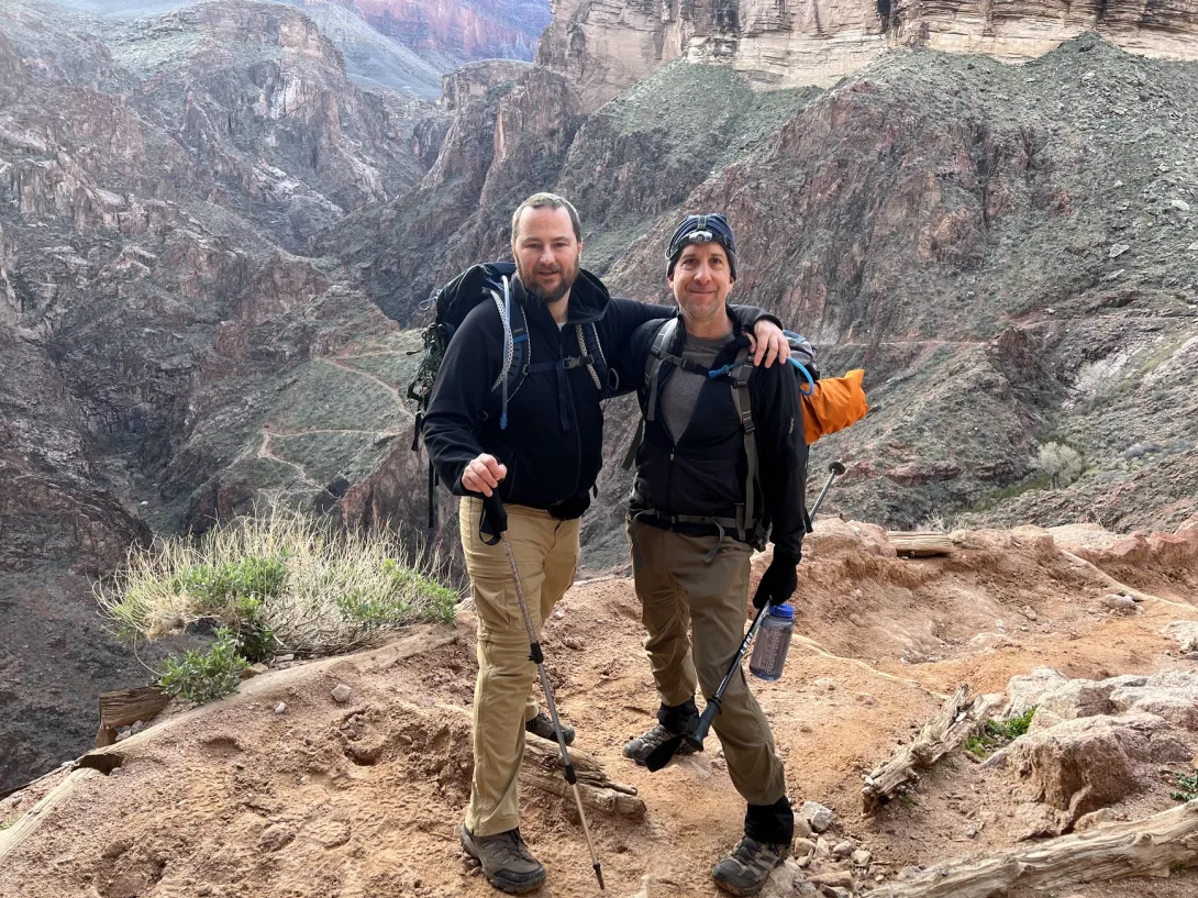 Two people posing on a trail with arm over each others shoulders looking over the deep valley