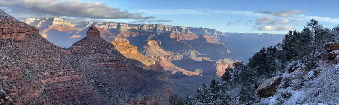 Panorama of the Grand Canyon showing sun on the ridge and snow at the tops