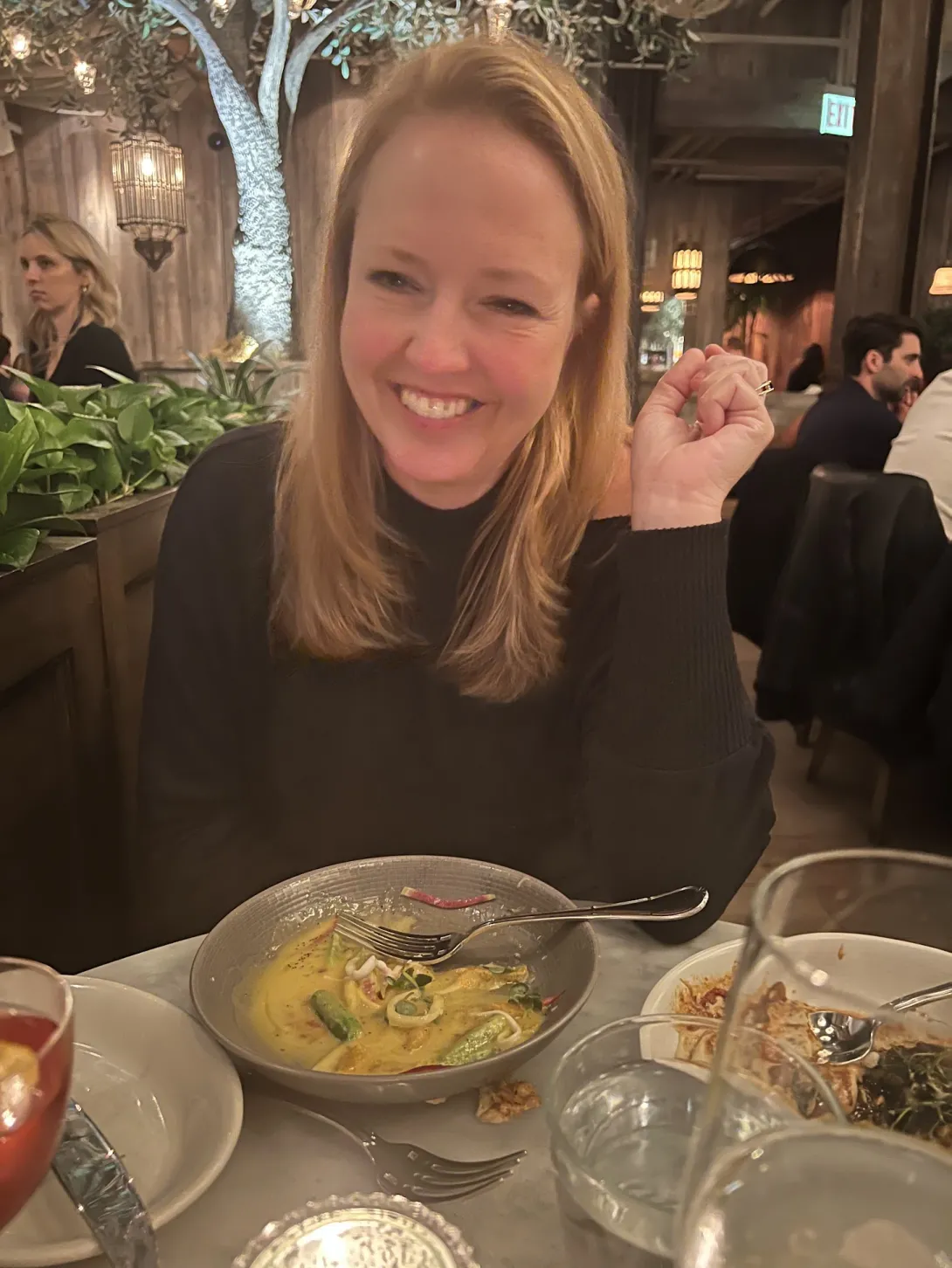 Robin smiling beautifully in front of some half eaten food in a dimly lit restaurant