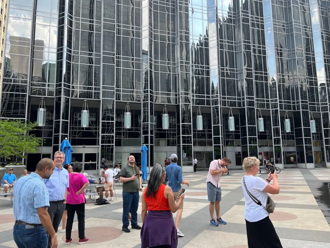 Board members standing around next to huge glass walled buildings looking around and taking pictures