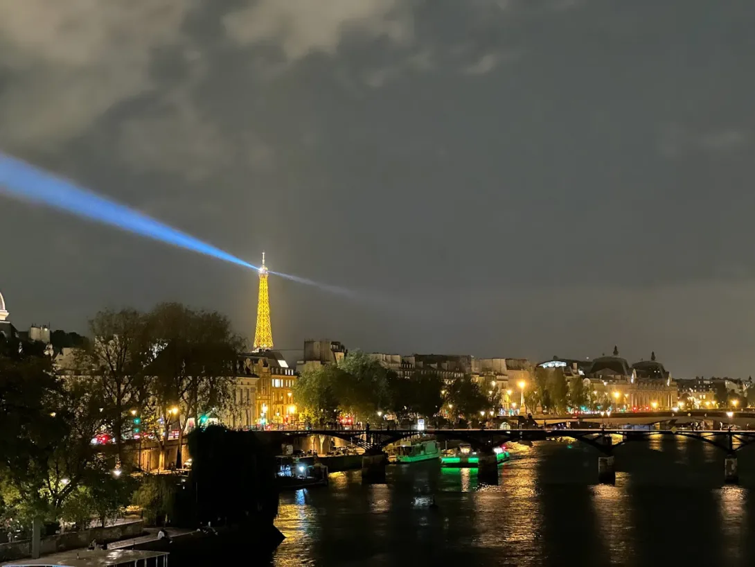 View of the Eiffel Tower in the distance at night with it's search lights scanning