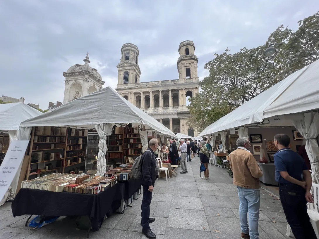 Looking down the isle of a flea market in Paris with a tent with books in the foreground and a church in the distance