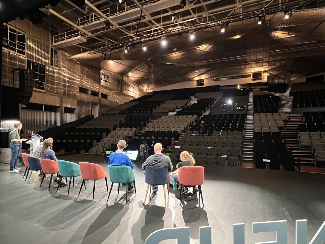 Shot from behind, several speakers in chairs in front of large empty auditorium