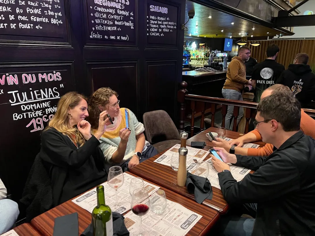 Several people screwing around with phones at a dinner table with wine and menus on the table